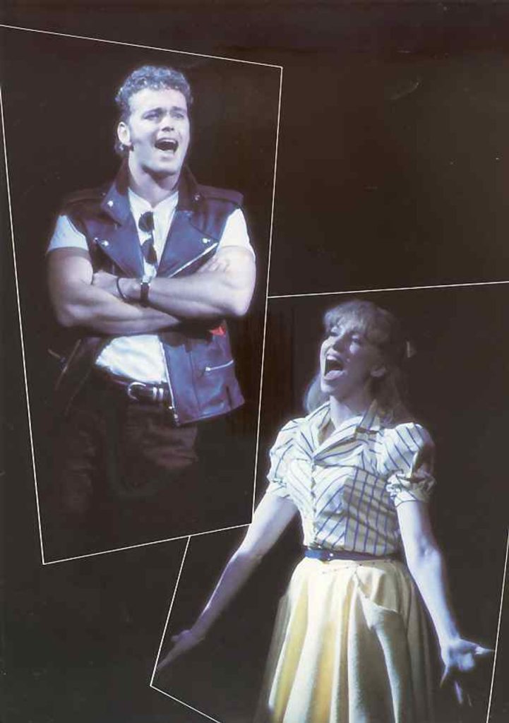 Craig McLachlan singing a duet on a split screen in Grease The Arena Spectacular.